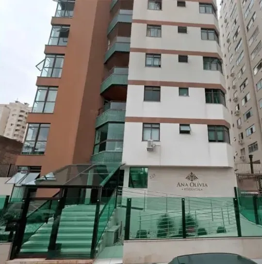 Fachada del Edifício Residencial Ana Olívia, edificio alto en tonos beige y terracota con balcones vidriados y entrada con escalera de vidrio verde