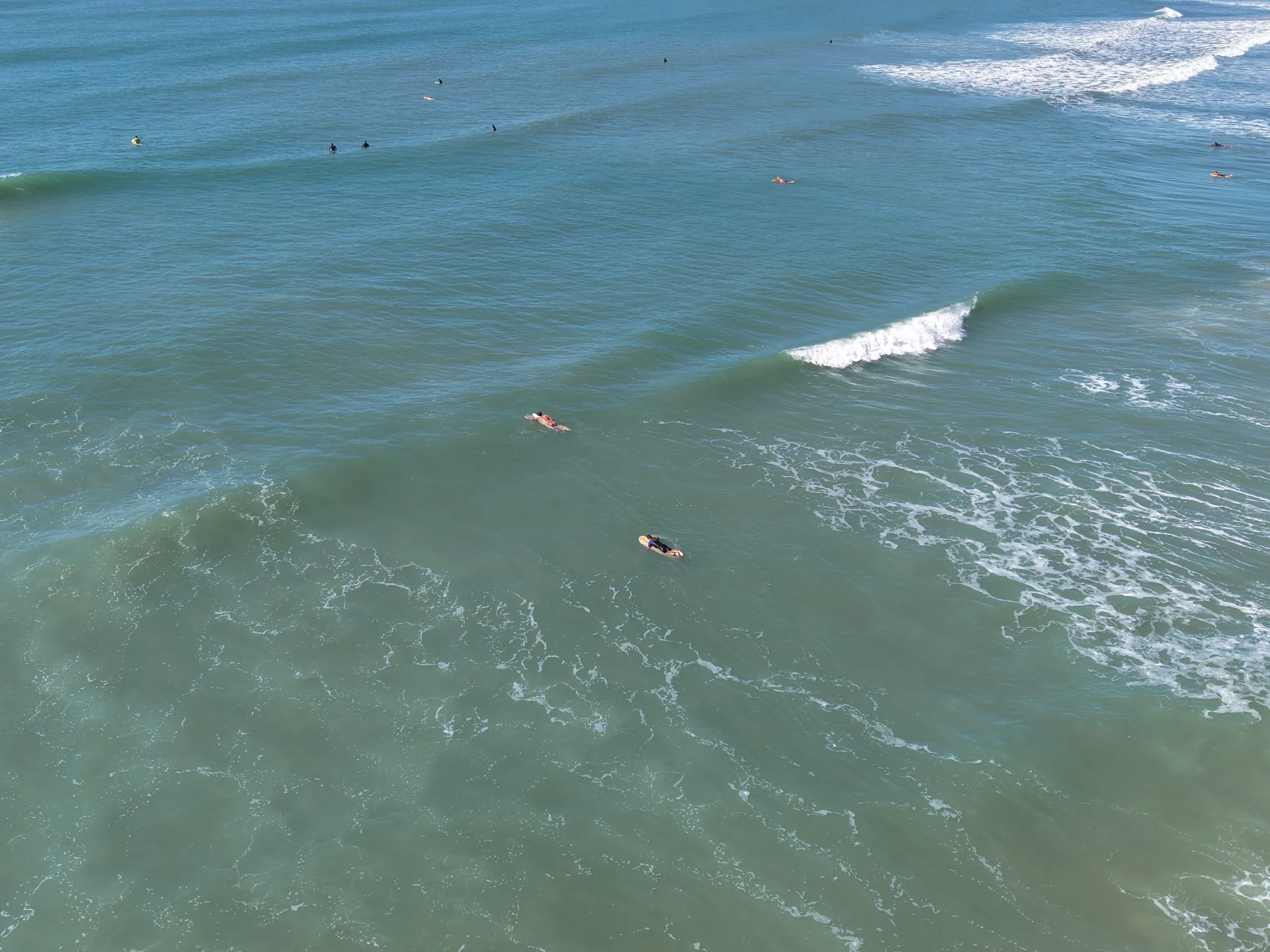 Vista aérea de surfistas no mar, com ondas quebrando sobre a água verde-azulada